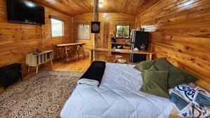 L’intérieur d’un chalet confortable, avec un lit, un téléviseur, un jeu de fléchettes, un petit coin cuisine et une fenêtre.