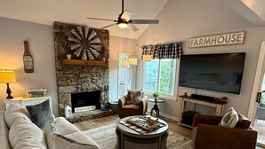 Un salon chaleureux avec une cheminée en pierre, un grand téléviseur et des fauteuils confortables.