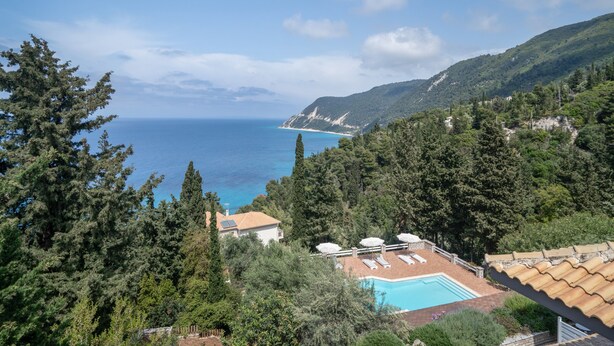 Una piscina con sillones de descanso, vista al mar y un paisaje montañoso.