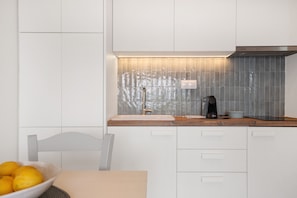 A modern kitchen with white cabinets, a wooden countertop, and a tiled backsplash.
