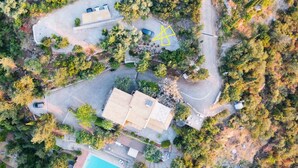 An aerial view of a property with a swimming pool, a large building, and surrounding trees.