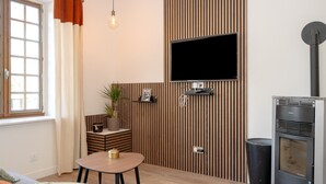 Ett modernt vardagsrum med en platt-TV, en väggpanel i trä, en öppen spis, ett litet bord och ett fönster med gardiner.
