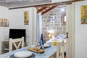 A dining area with a table set for two, a television, and a stone wall in the background. - Holiday Home 'Laura' with Shared Pool, Wi-Fi and Air Conditioning (Conil de la Frontera)