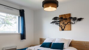Una cama bien hecha con ropa de cama blanca y aguamarina, un cabecero de madera y una obra de arte de un árbol colgada en la pared.