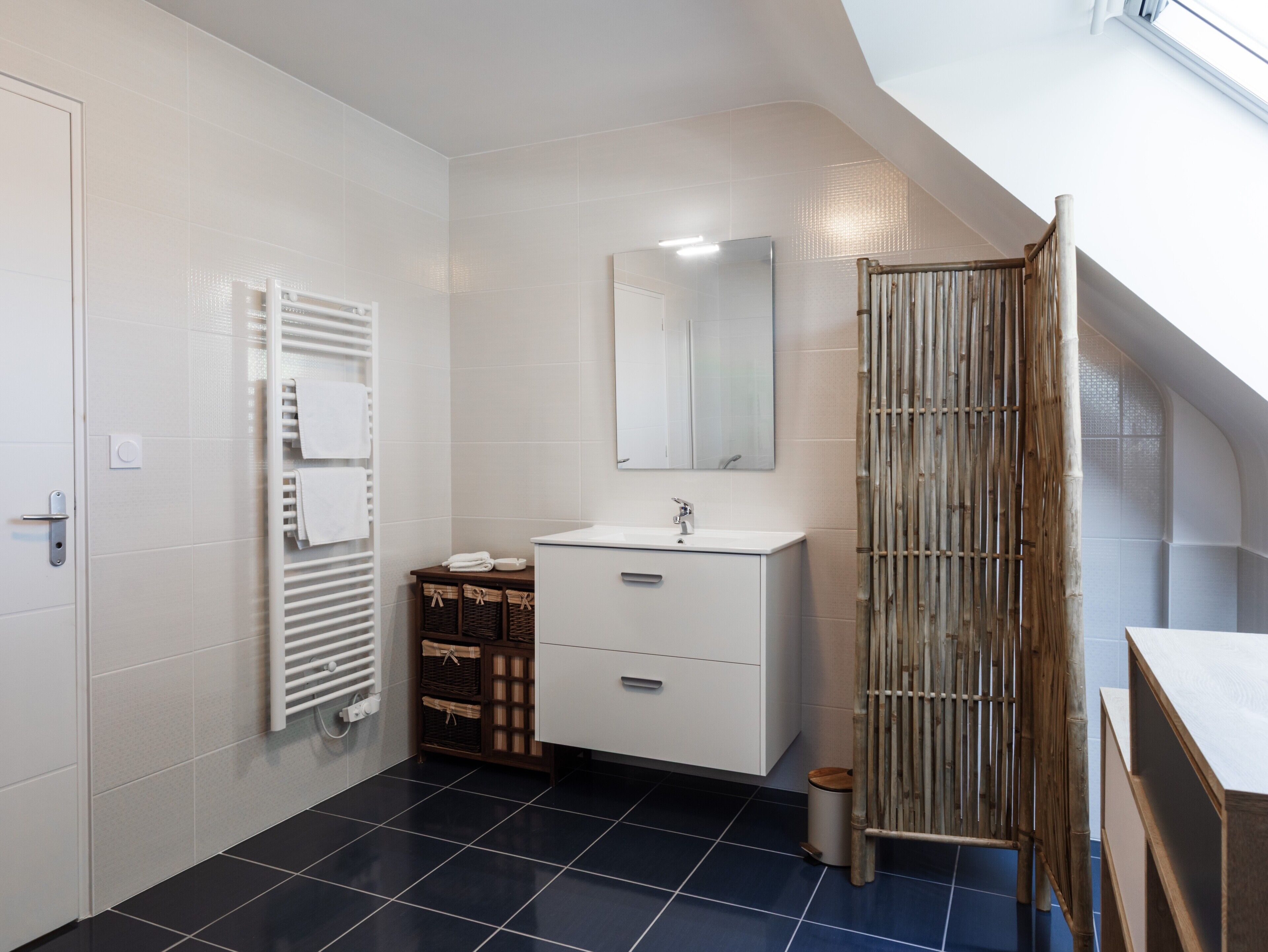 Un bagno con un mobile lavabo bianco, uno specchio, un porta asciugamani e un box doccia in bambù.