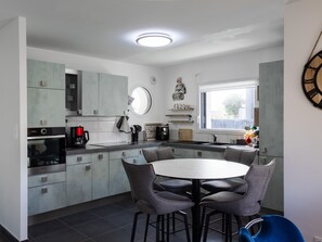 A modern kitchen with grey cabinets, a round dining table, and bar stools.