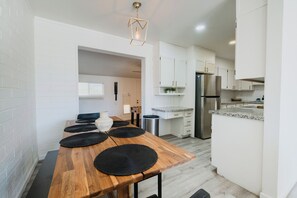A modern kitchen with white cabinets, a stainless steel refrigerator, and a wooden dining table with black placemats.