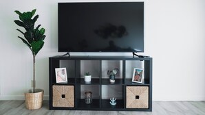 Een zwarte tv-meubel met een flatscreen televisie, een potplant en decoratieve objecten.