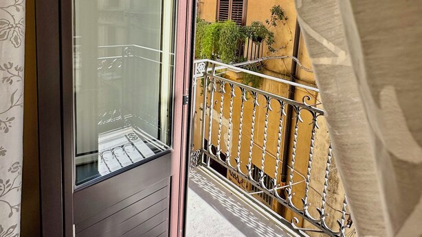 Ein Balkon mit Metallgeländer, eine Tür mit Glasscheibe und ein Gebäude mit gelbem Putz und Fensterläden.