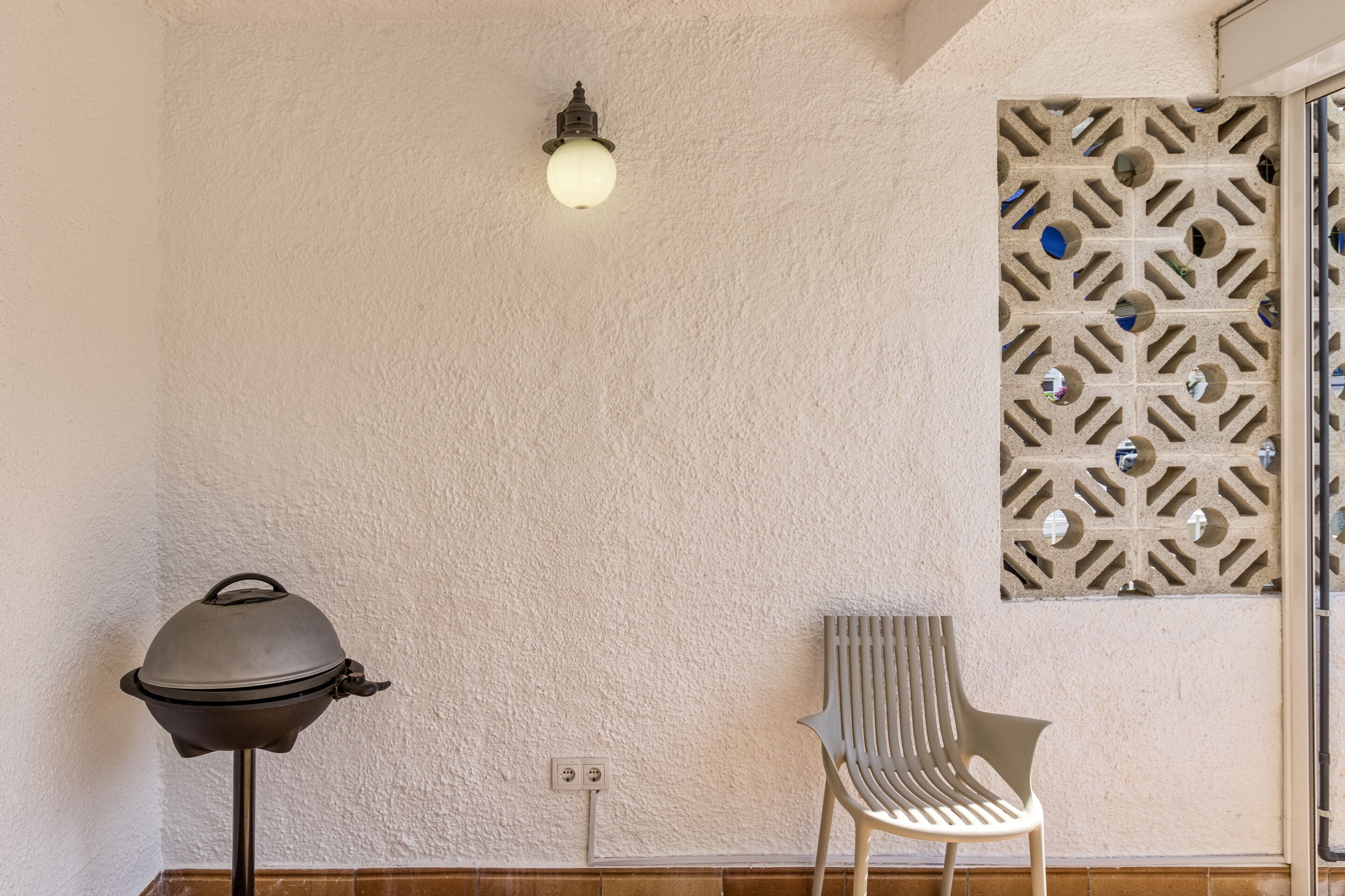 A room with a grill, a chair, a wall-mounted light fixture, and a decorative panel.