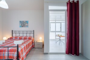 A bedroom with a bed, bedside lamps, a nightstand, a window with a view, and a red curtain. - Room 'Leverblu  5' with Shared Terrace, Wi-Fi and Air Conditioning (Avola)
