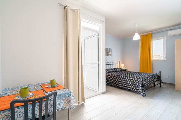 A room with a bed, a table with two chairs, a window with curtains, and a hanging light fixture.
