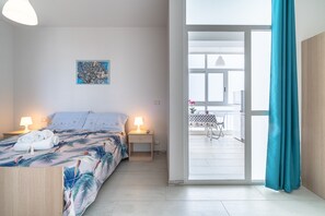 Une chambre à coucher avec un lit, des lampes de chevet, une table de chevet, un tableau et une vue sur un balcon extérieur.