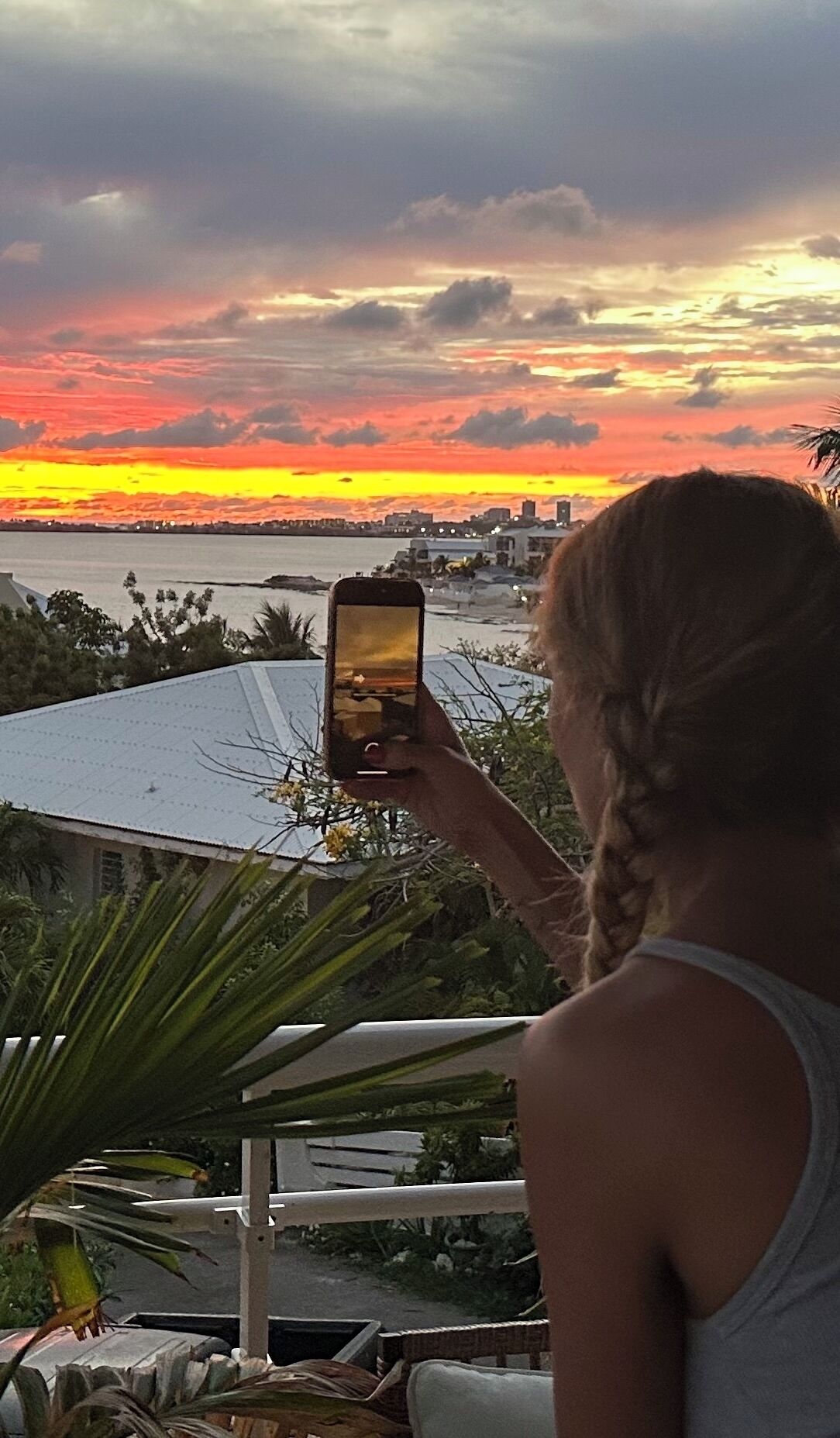 Une personne prend une photo d’un coucher de soleil, avec la silhouette d’une ville en arrière-plan.