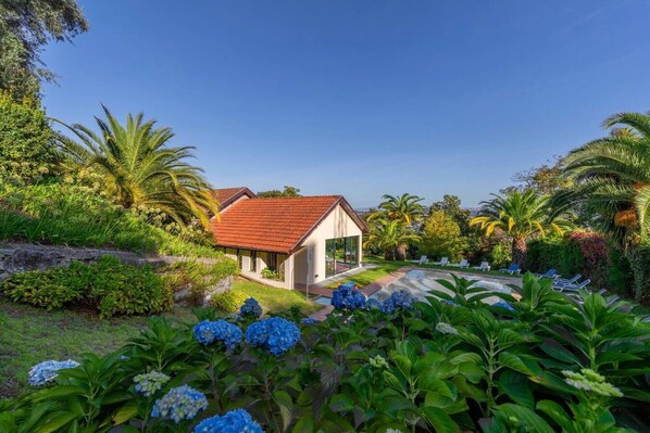 A house with a red roof, surrounded by lush greenery and a swimming pool.