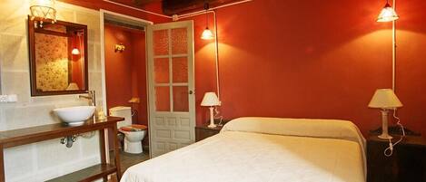 Un dormitorio con una cama, mesita de noche, espejo, lavabo e inodoro.
