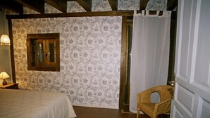 Un dormitorio con una cama, una silla, un ventanal de madera y papel tapiz estampado.