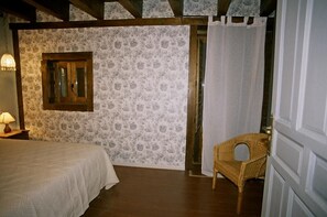 Ein Schlafzimmer mit Bett, Stuhl, einem Fenster mit Holzrahmen und gemustertem Wandpapier.
