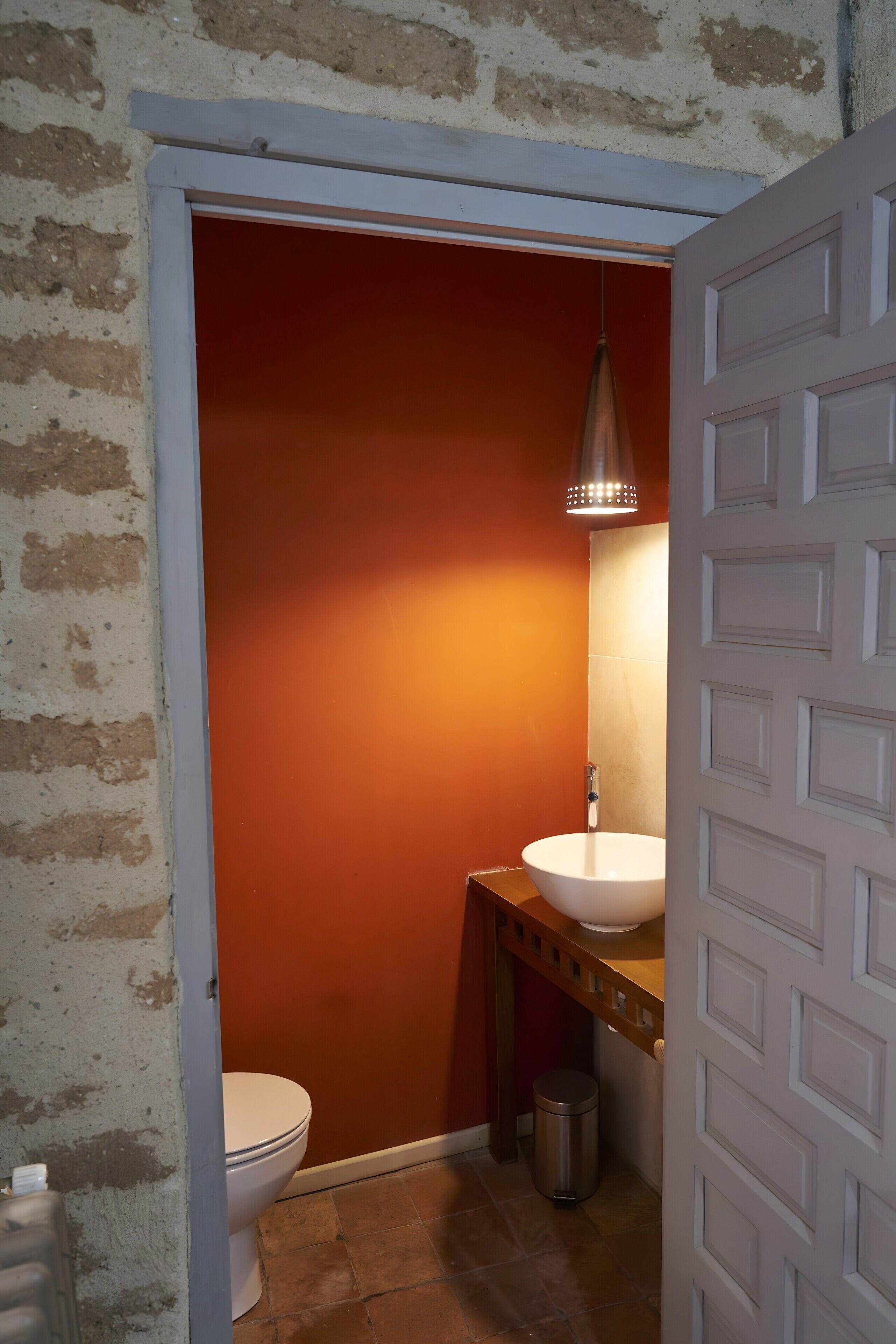 Une salle de bain avec des toilettes blanches, un meuble-lavabo en bois, un lavabo blanc et un luminaire suspendu.
