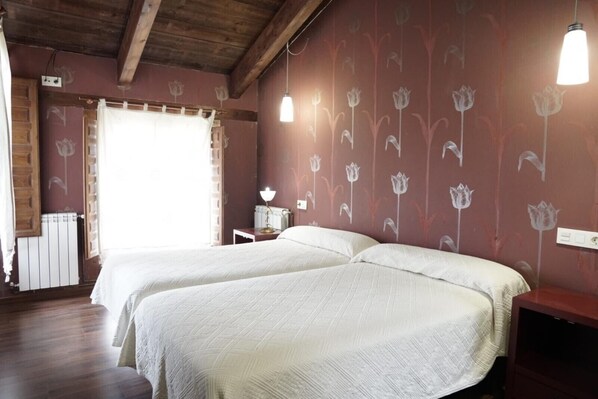 Habitación con dos camas, vigas de madera en el techo, un radiador y una pared con estampado floral.