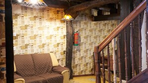 A cozy room with a wooden staircase, a quilted sofa, patterned wallpaper, and a fire extinguisher.