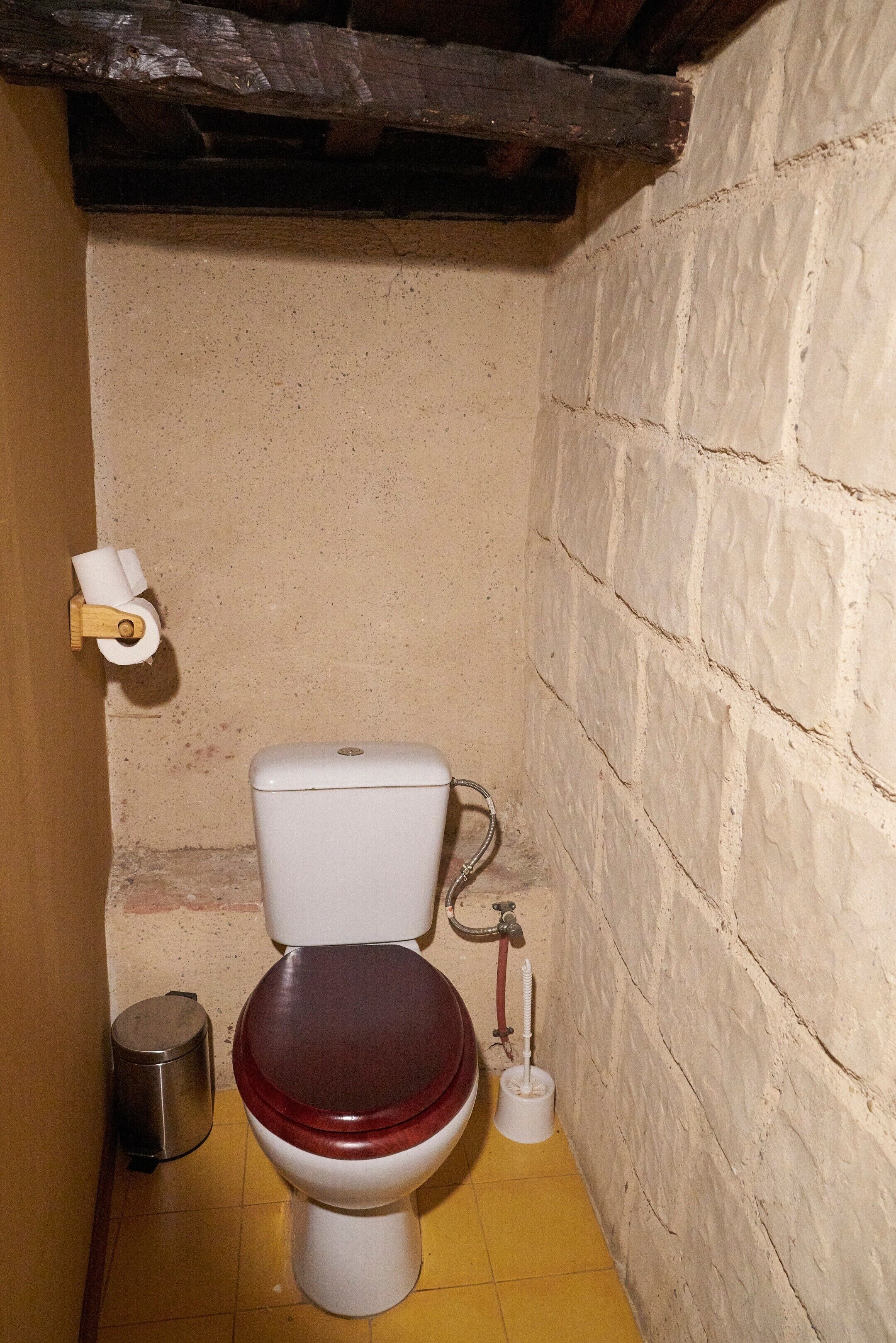 Un baño pequeño y estrecho, con un inodoro blanco, suelo de madera y pared de ladrillo.