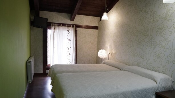 A bedroom with two beds, a radiator, a window with curtains, and a wall with a floral pattern.