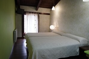 Un dormitorio con dos camas, un radiador, una ventana con cortinas y una pared con estampado floral.