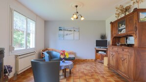Ein Wohnzimmer mit einer Couch, einem Tisch mit einer Vase, einem Holzschrank und einem Fernseher.