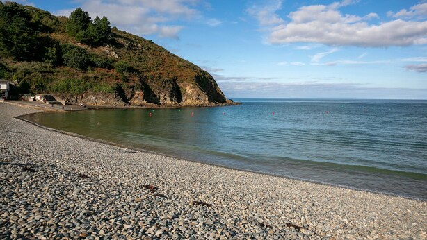 Ein Kiesstrand mit einer felsigen Klippe und ruhiger See.
