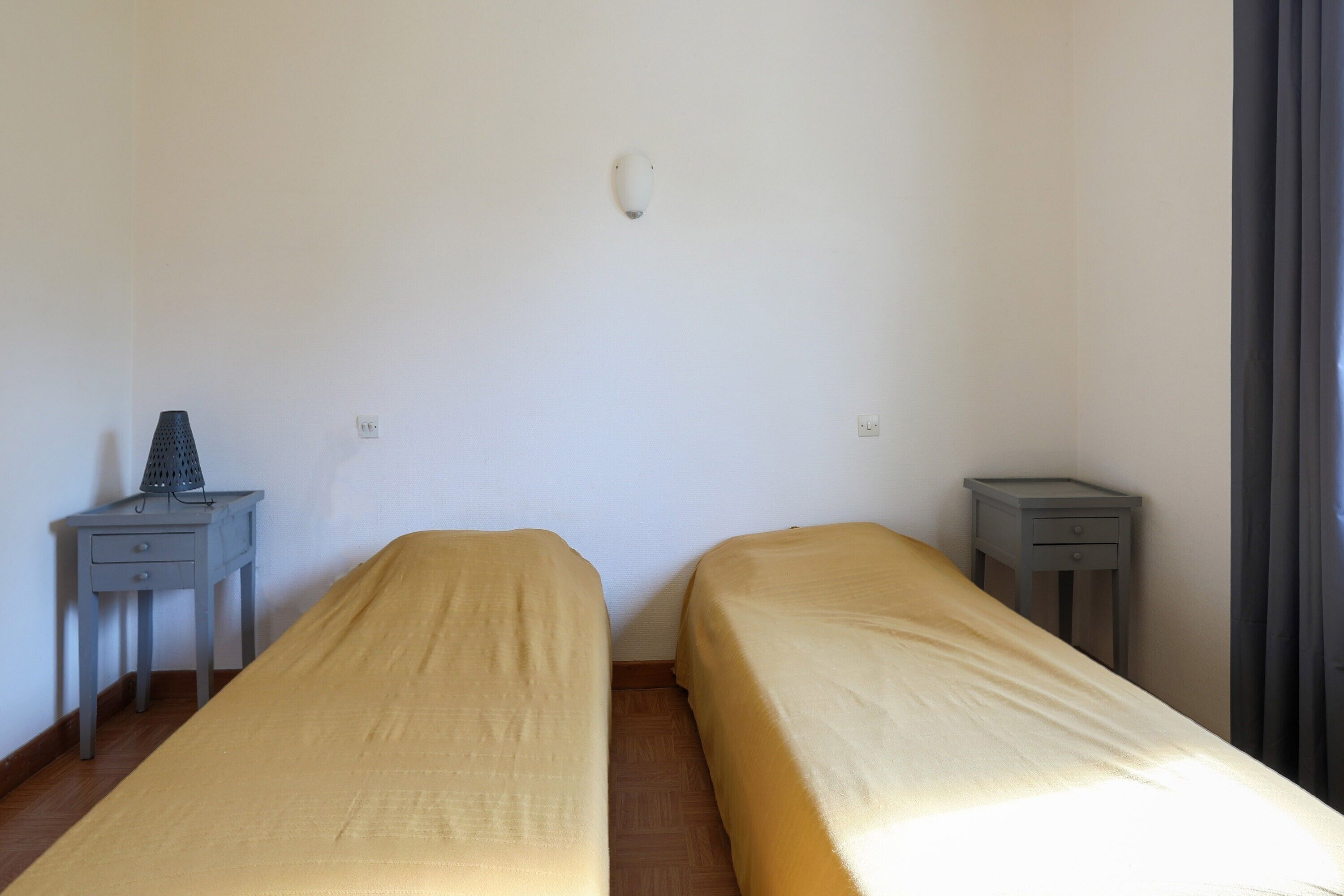 A room with two single beds, a small table with a lamp, and a nightstand.