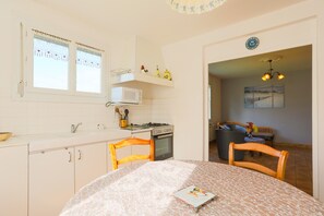 A kitchen with a microwave, stove, and cabinets, a dining table with chairs, and a window with curtains. - Holiday Home 'Maison Plouha Proche Plage' with Private Terrace and Private Garden (Plouha)