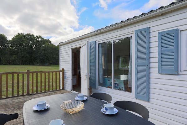 Une terrasse avec une table et des chaises, une clôture en bois et une maison aux volets bleus.
