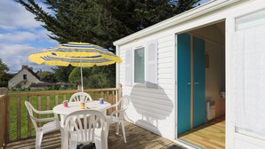 A deck with a table and chairs, an umbrella, and a door to a room. - Mobile Home 'Bikini' with Private Terrace and Private Garden (Plouha)