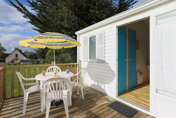 Une terrasse avec une table et des chaises, un parasol et une porte donnant sur une pièce.