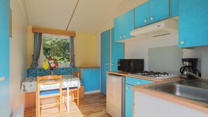 A compact kitchen with blue cabinets, a refrigerator, a microwave, a gas stove, and a sink. - Mobile Home 'Bikini' with Private Terrace and Private Garden (Plouha)
