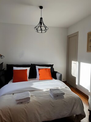 Une chambre à coucher avec un lit, des oreillers, un luminaire suspendu, une porte et une fenêtre.