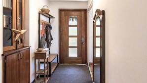 A hallway with a wooden door, a bench, a shelf with books and a star decoration, and a mirror on the wall.