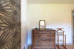 Une commode en bois avec des tiroirs et un miroir, un cintre en bois et un mur orné d’un motif.