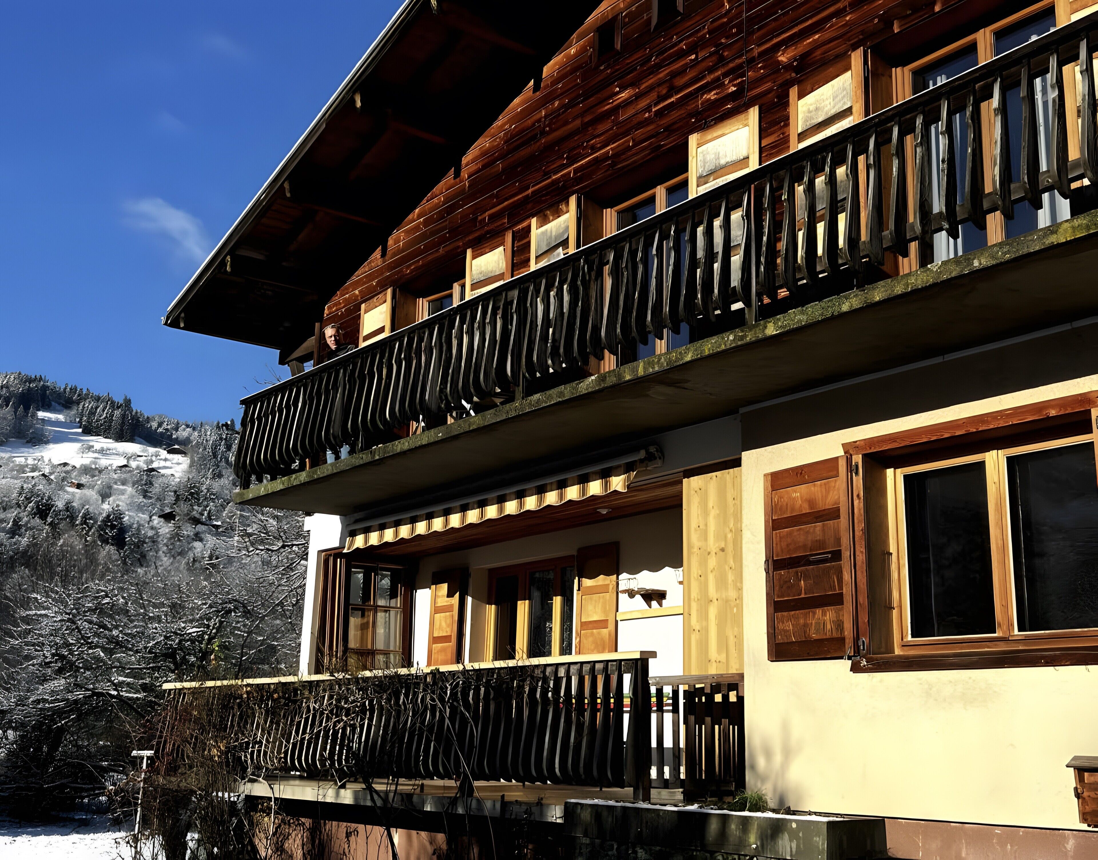 Un bâtiment en bois à deux étages, doté de balcons et de grandes fenêtres, avec un paysage enneigé en arrière-plan.