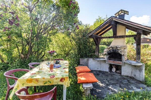 Un espace de restauration en plein air avec une table dressée pour deux personnes, un four en pierre et une pergola en bois.