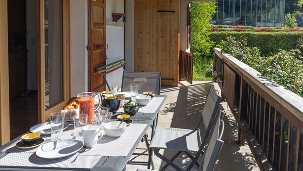 A dining area with a table set for two, a wooden door, and a view of greenery.