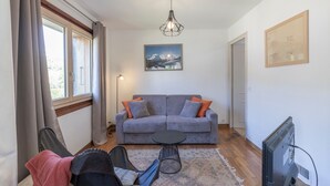 A living room with a grey sofa, a small round table, a TV, and a painting on the wall.
