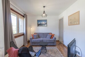 A living room with a grey sofa, a small round table, a TV, and a painting on the wall.