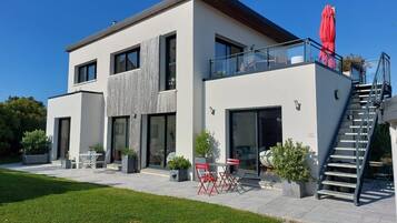 A modern two-story house with a balcony, outdoor seating, and a staircase.