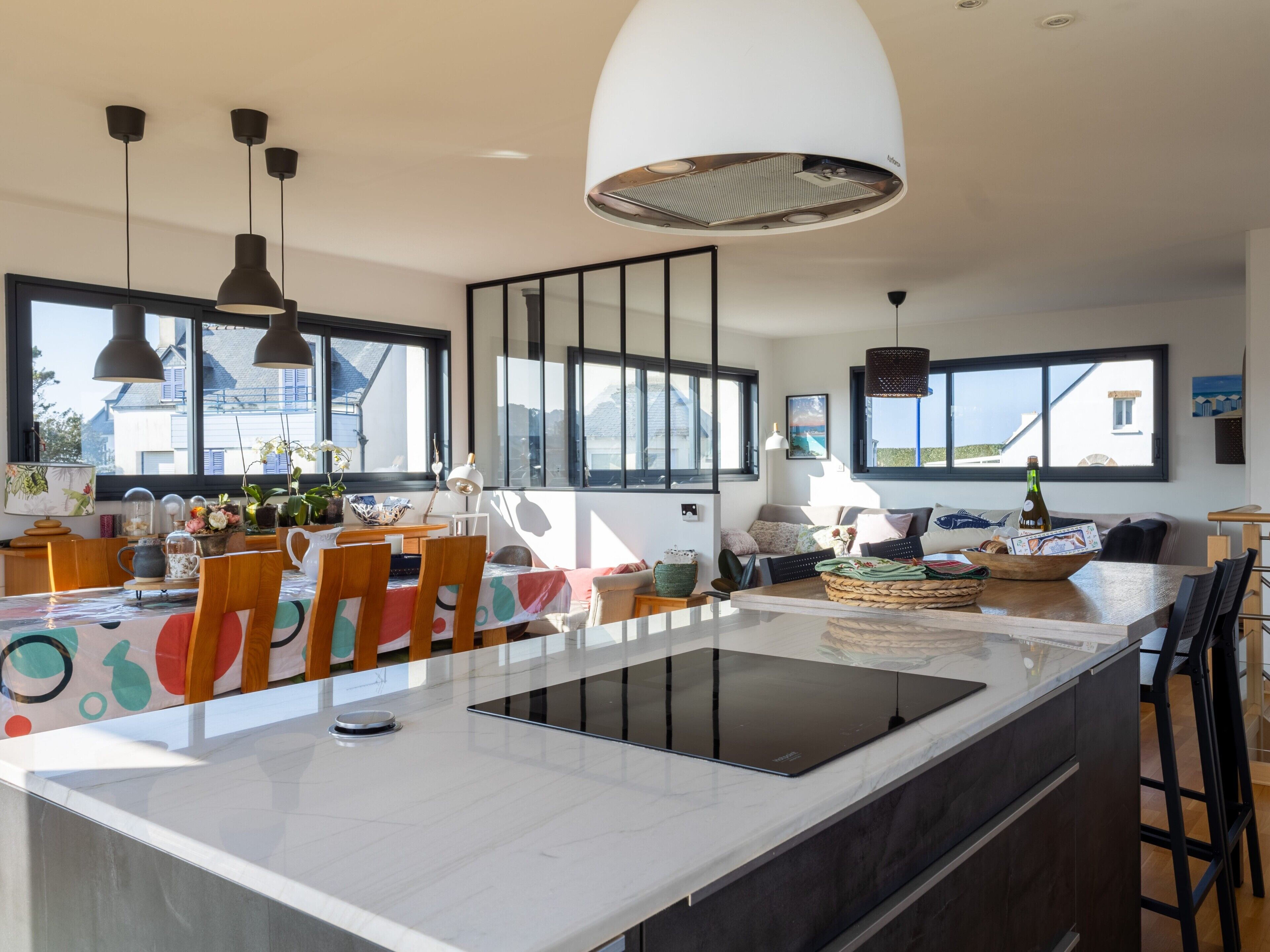 A modern kitchen with a central island, pendant lighting, and large windows.