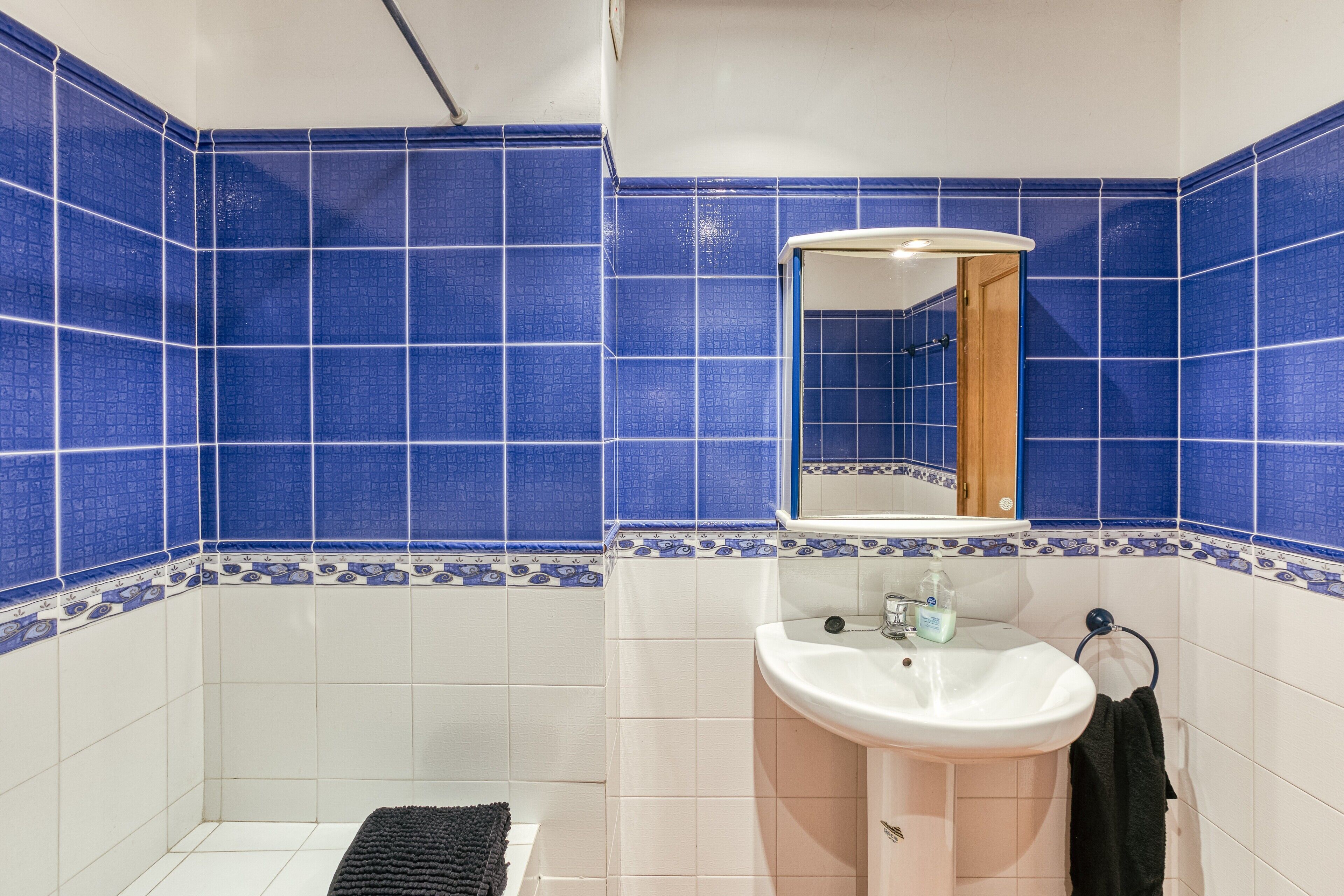 A bathroom with blue and white tiles, a sink, a mirror, and a towel rack.