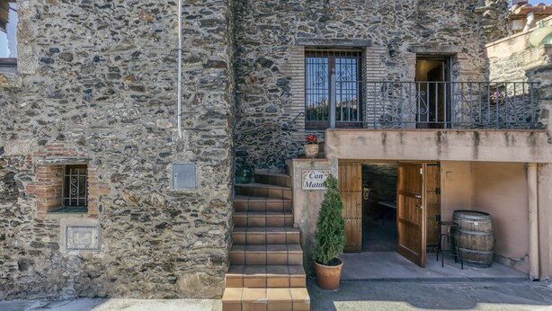 A stone building with a wooden door, a balcony with metal railings, and a potted plant. - Country House 'Matalí' with Private Terrace, Wi-Fi and Air Conditioning (Espolla)