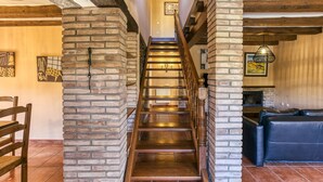 A staircase with wooden railings and brick walls, leading to a living area with a sofa and a fireplace. - Country House 'Matalí' with Private Terrace, Wi-Fi and Air Conditioning (Espolla)