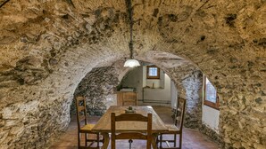 A stone-walled dining area with a wooden table and chairs, a hanging light fixture, and a window with a view. - Country House 'Matalí' with Private Terrace, Wi-Fi and Air Conditioning (Espolla)